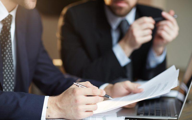 Closeup portrait of two unrecognizable  business partners reviewing paperwork and signing contract papers at table during meeting